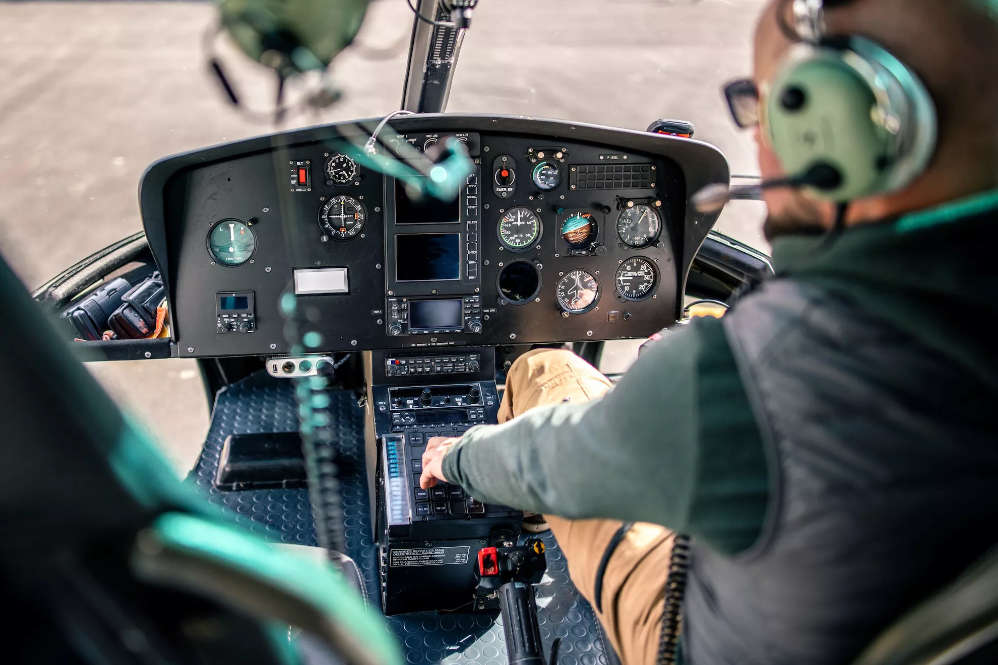 A close-up view of a helicopter cockpit with a pilot operating the controls. The dashboard features various gauges and instruments, with the pilot wearing a headset and adjusting the controls. The scene emphasizes precision and aviation technology in a realistic setting. 