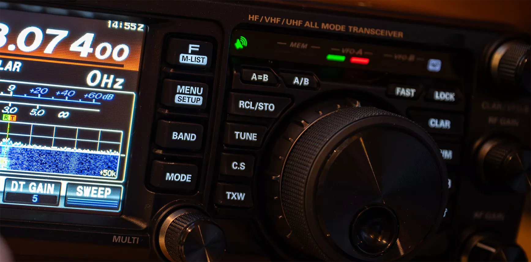 A close-up view of an HF/VHF/UHF all-mode transceiver, showing detailed buttons, a frequency display, and illuminated indicators. The image highlights the precision and technology used in advanced communication equipment. 